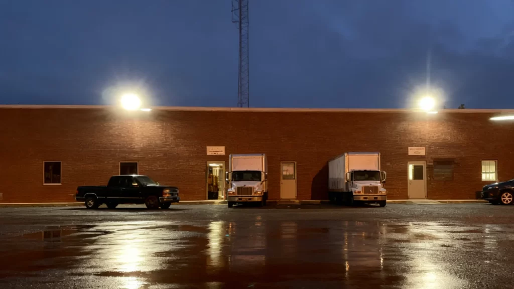 Night view of a Phoenix industrial park warehouse yard with trucks and containers, illuminated by Casyoo Helios Max all-in-one solar street lights.