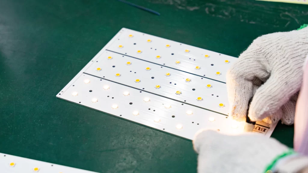Worker testing an LED light board on a green workbench, with multiple LED chips illuminated during quality inspection.